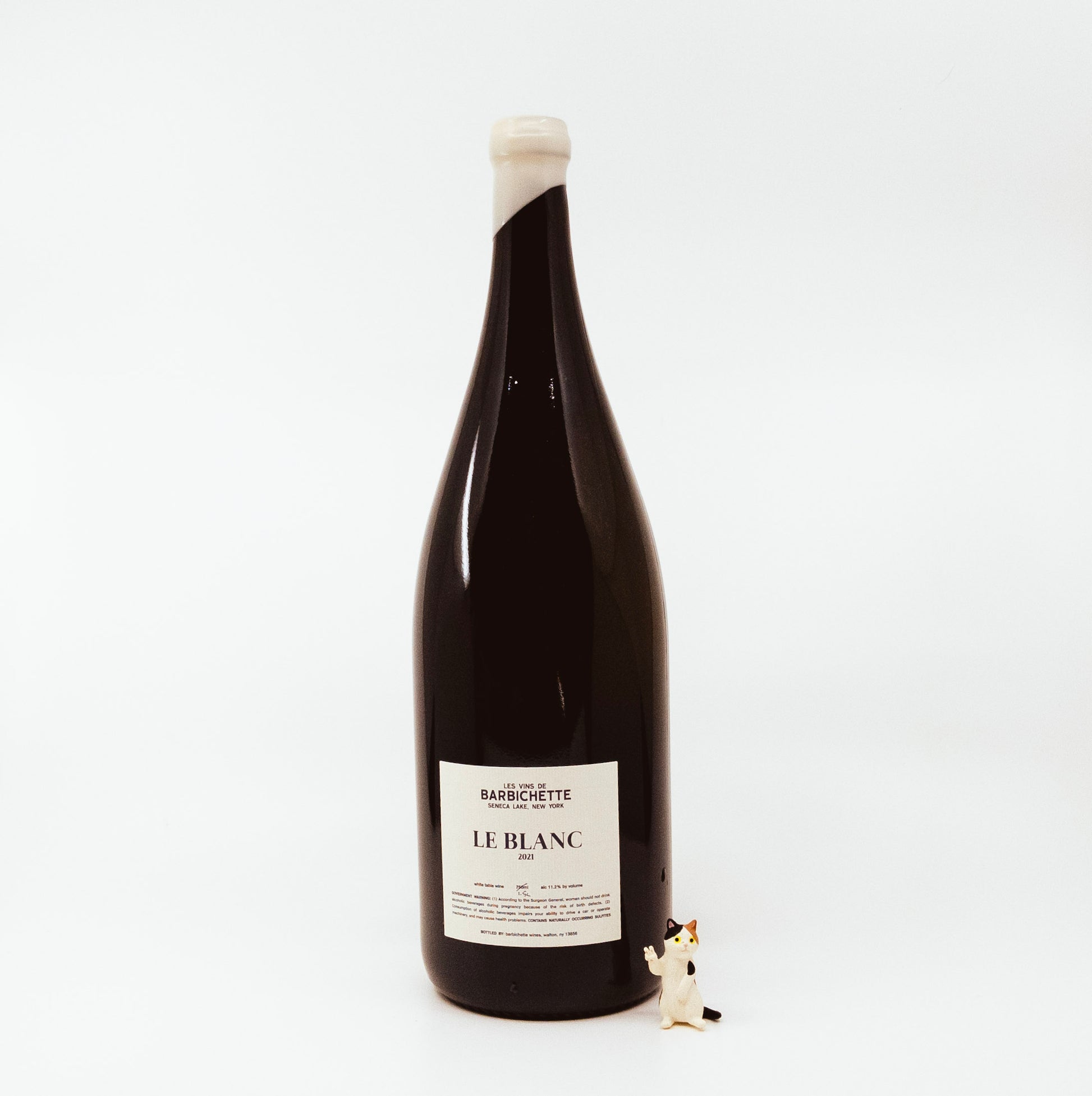 back of black wine bottle with white topper and white label next to cat figurine