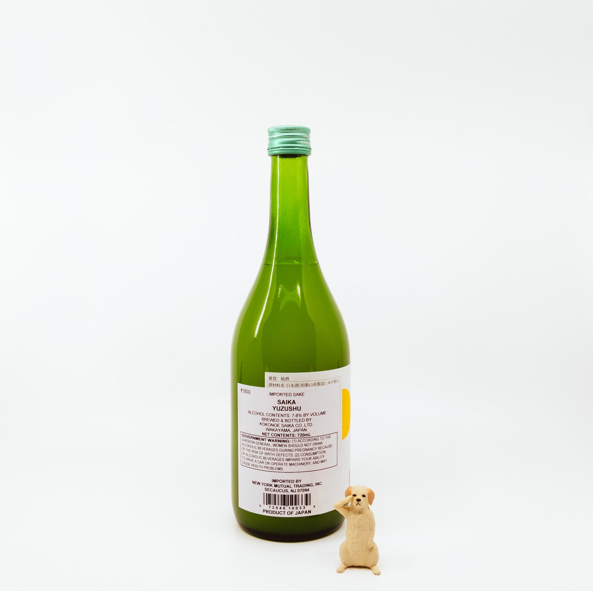back of green glass bottle with yellow on white label next to dog figurine