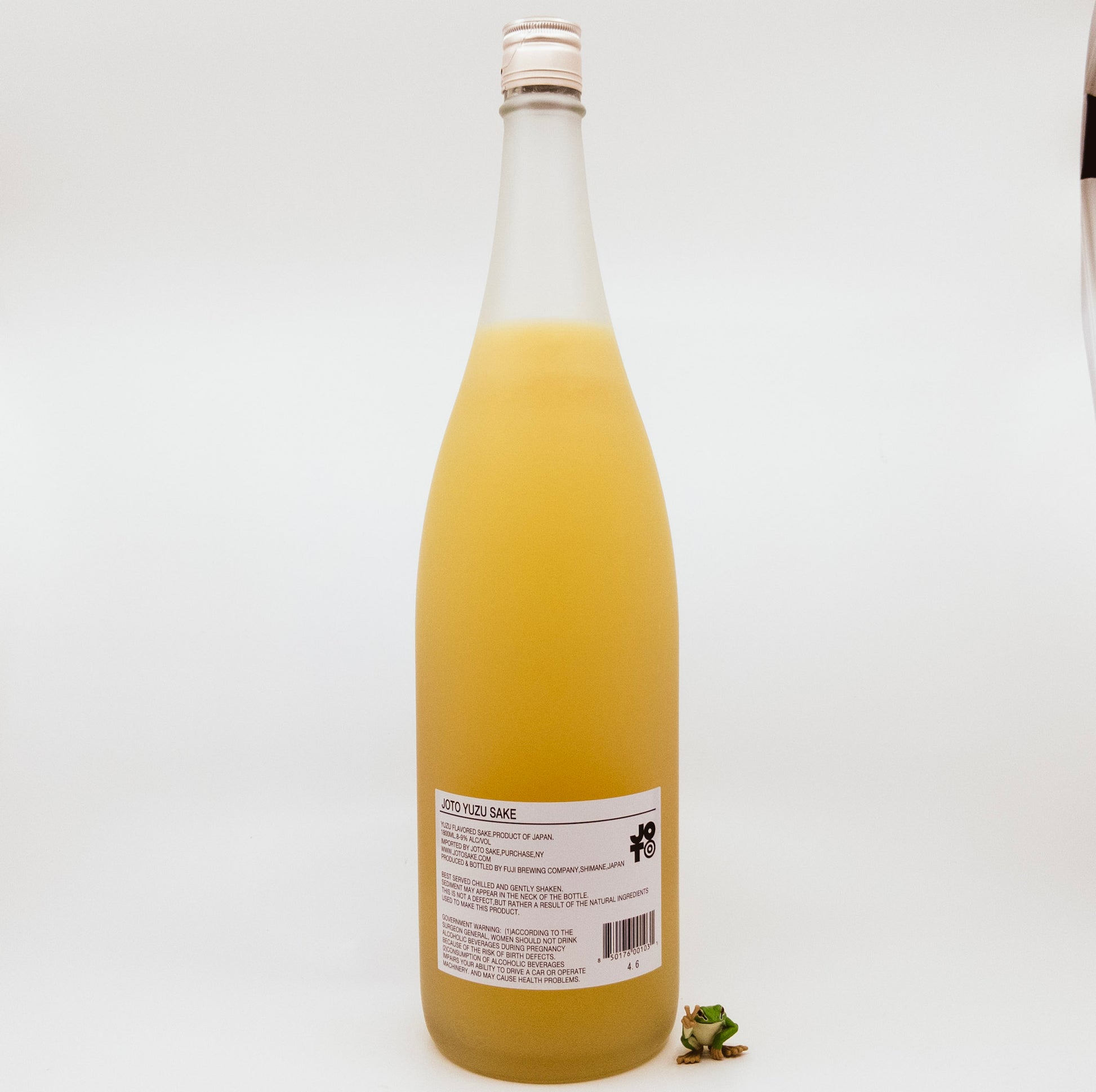 back of orange bottle with orange flower on label next to frog figurine