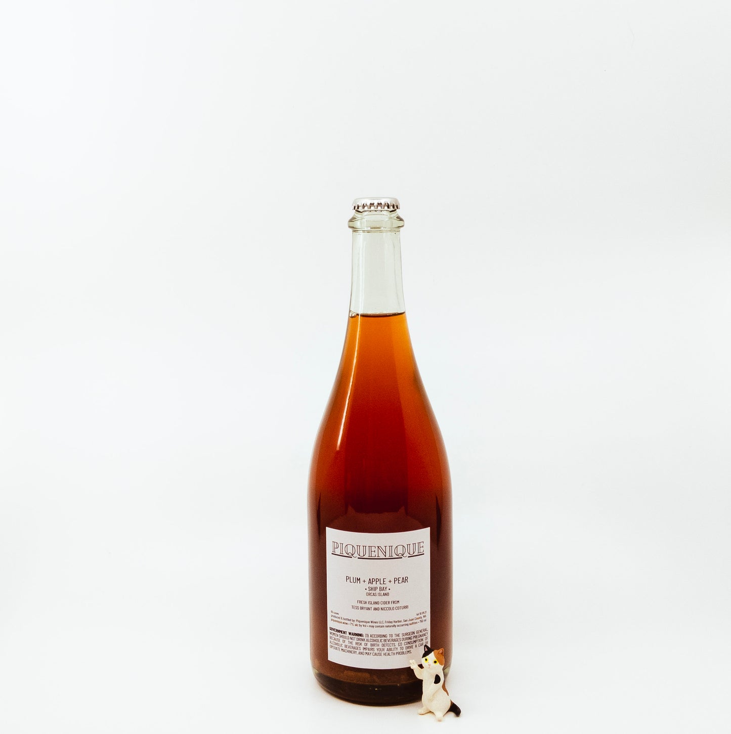back of red glass bottle with scenic label next to cat figurine