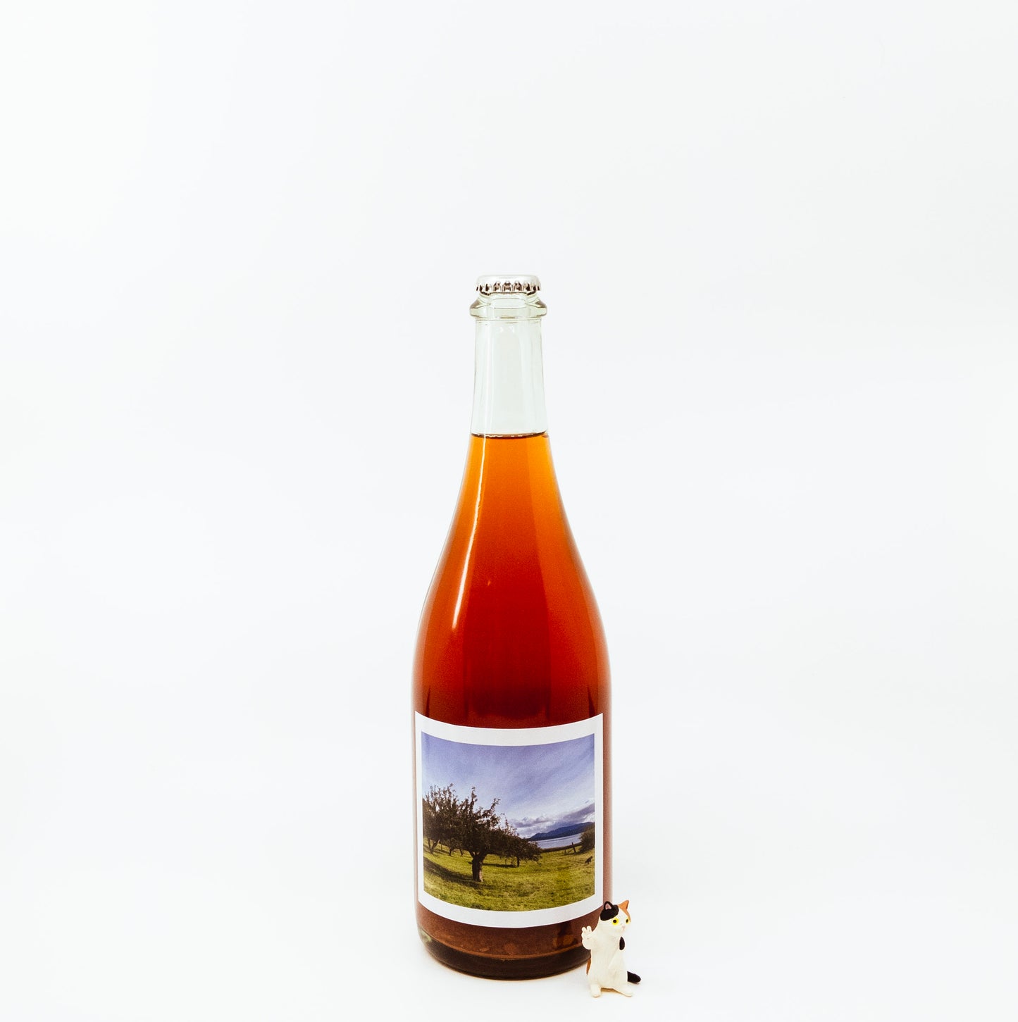 red glass bottle with scenic label next to cat figurine