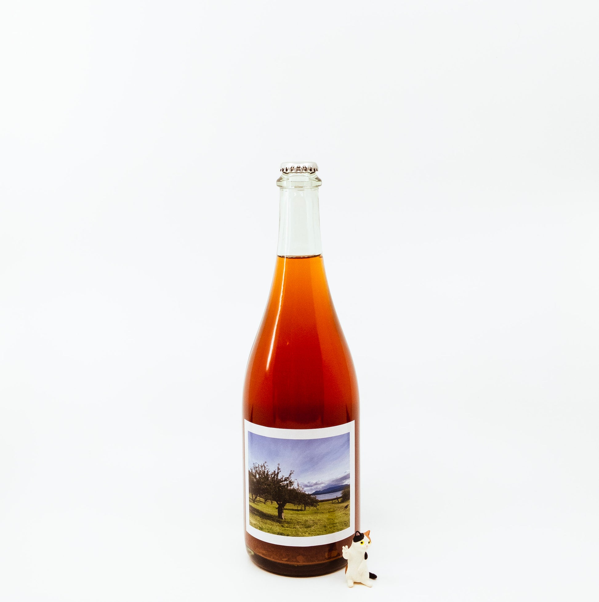 red glass bottle with scenic label next to cat figurine