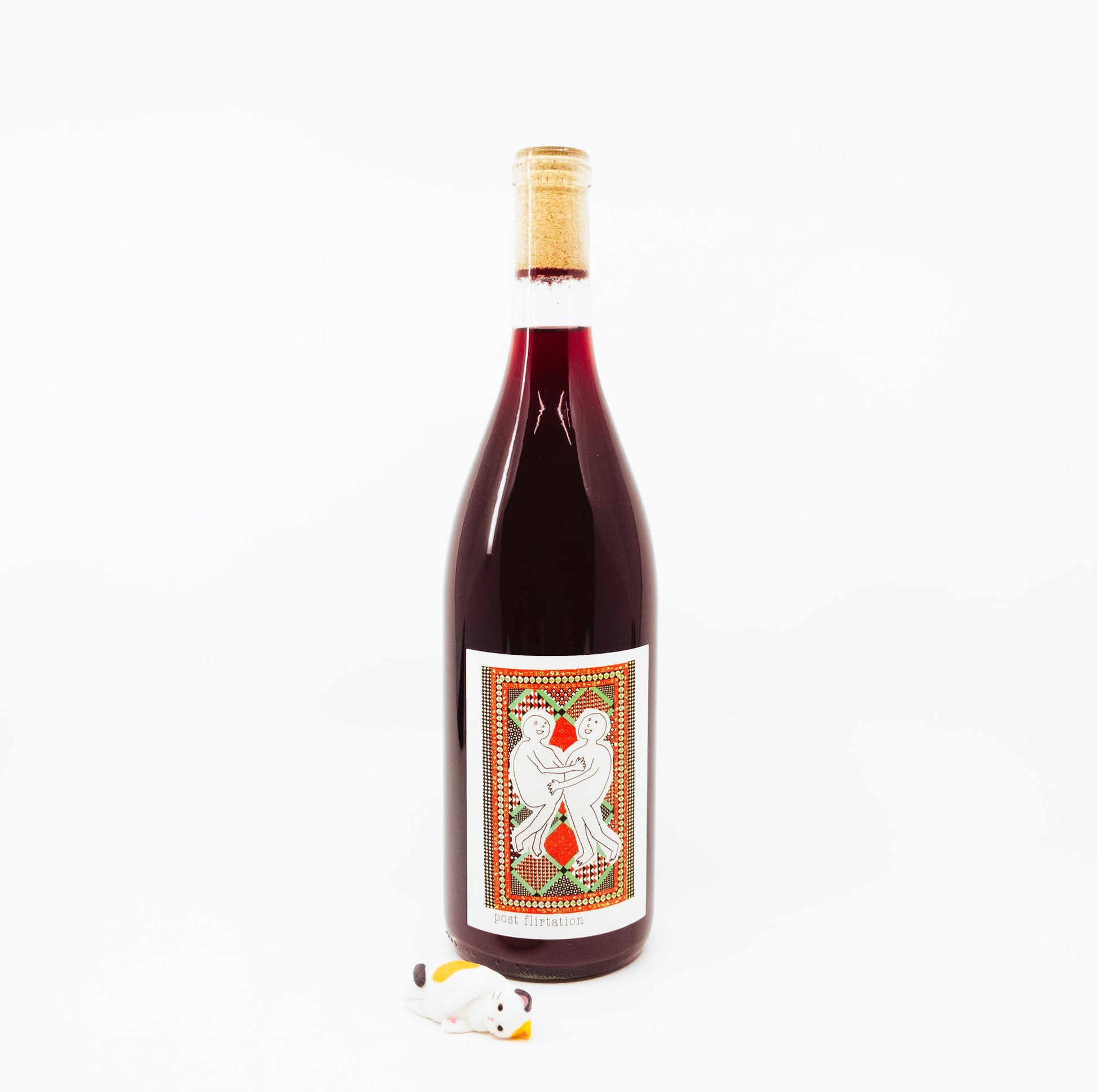 bottle with two people on colorful label next to cat figurine