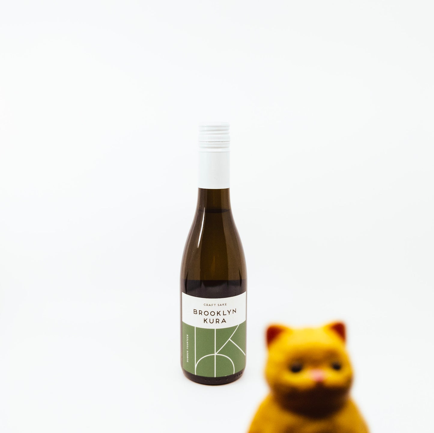small bottle of brooklyn kura with green label with cat figurine